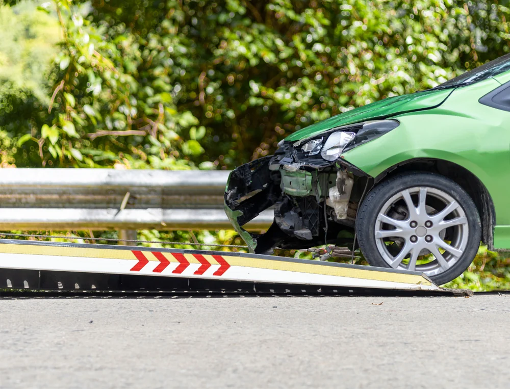 Damaged green car being loaded onto a tow truck after a collision — TKM Smash Repairs, Edmonton QLD