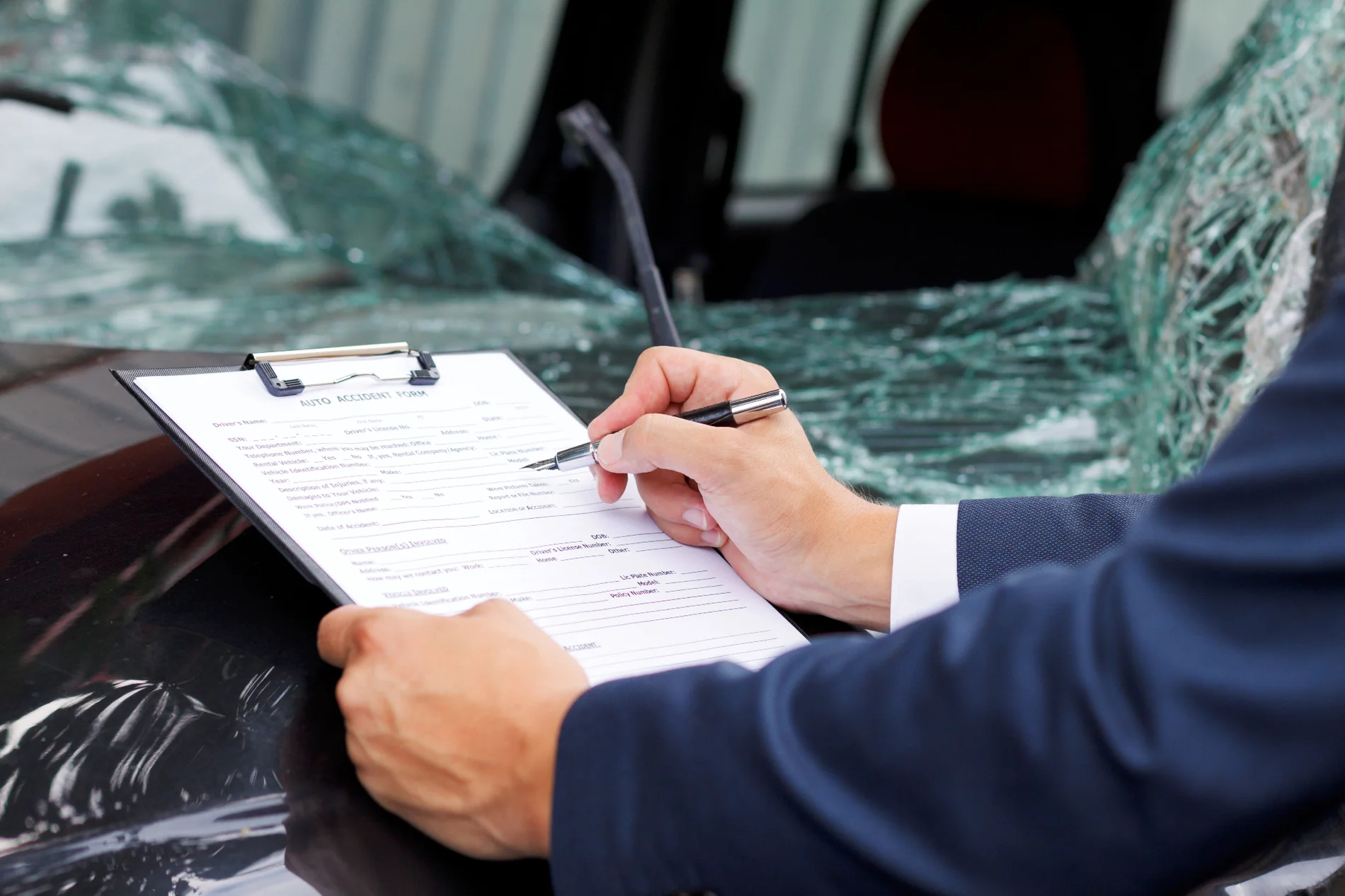 Person in suit filling out an auto accident insurance claim form beside a smashed windscreen — TKM Smash Repairs, Edmonton QLD