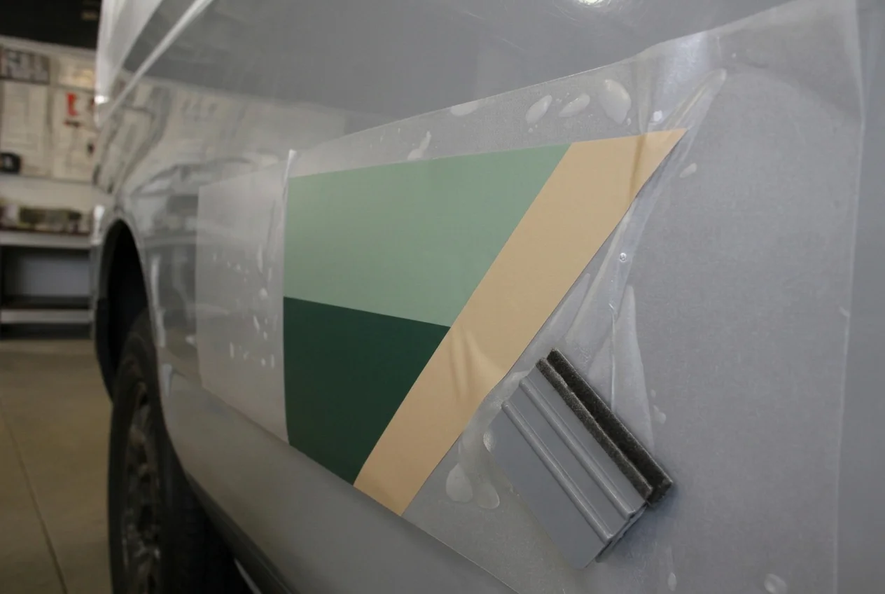 Vinyl signage decal being squeegeed onto a vehicle panel — TKM Smash Repairs, Edmonton QLD