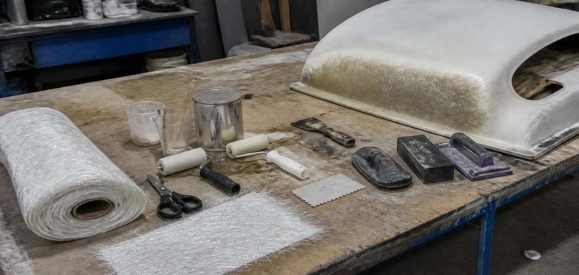 Fibreglass repair tools, matting and resin laid out across a workshop bench beside a panel — TKM Smash Repairs, Edmonton QLD