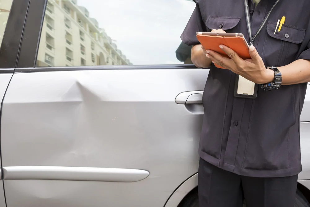 Insurance assessor inspecting a dented car door with a tablet — TKM Smash Repairs, Edmonton QLD